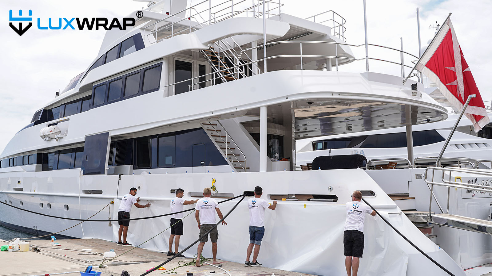 Expert wrappers install marine vinyl on a large yacht hull with white vinyl
