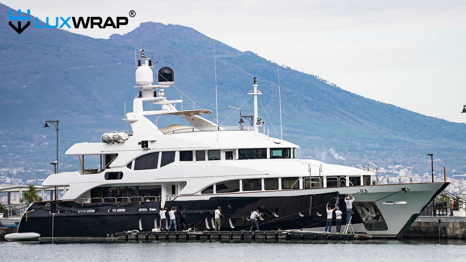 Team installs blue marine vinyl film on yacht hull from floating rafts