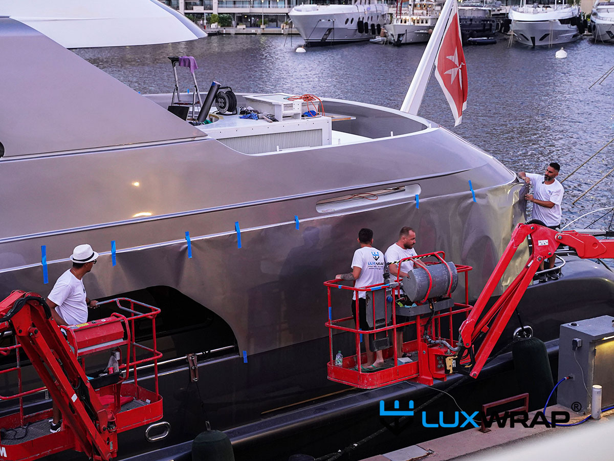 Cherry picker providing elevated access to wrap the exterior parts of a large superyacht superstructure in silver vinyl