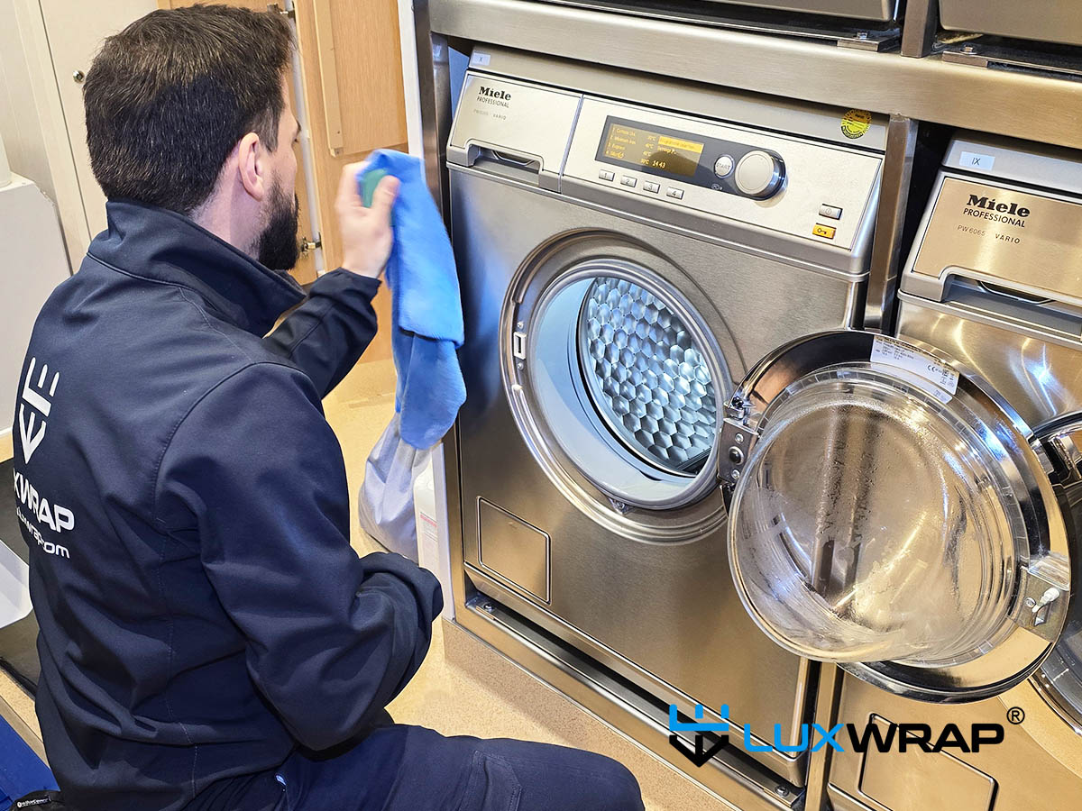 LuxWrap installer applying protective film to stainless steel panels in a superyacht laundry room