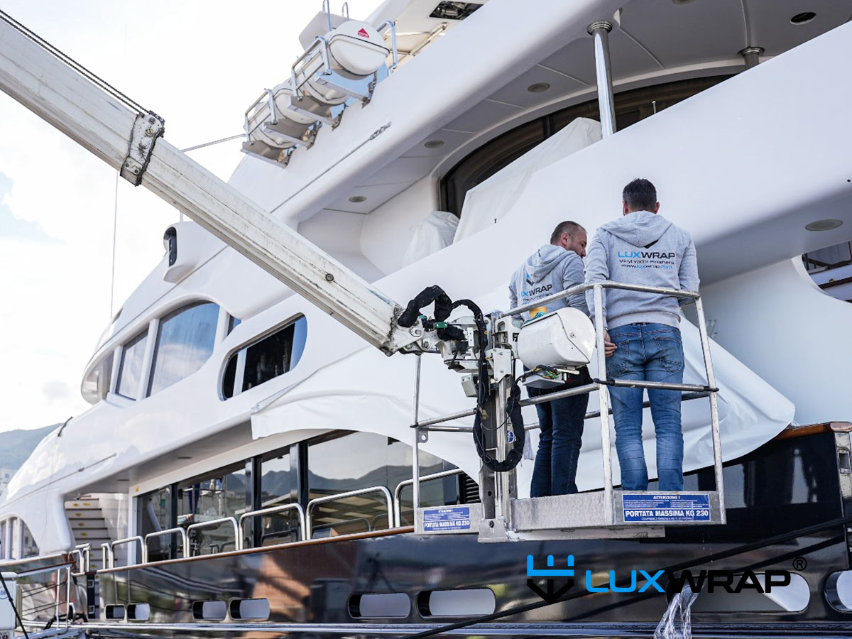 LuxWrap crew installing white vinyl on the exterior superstructure of a large yacht from a mechanical lift