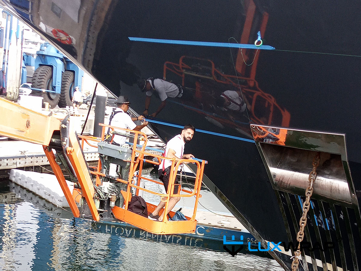 Large superyacht bow being wrapped with cherry picker access — standard practice on yachts above 40 metres